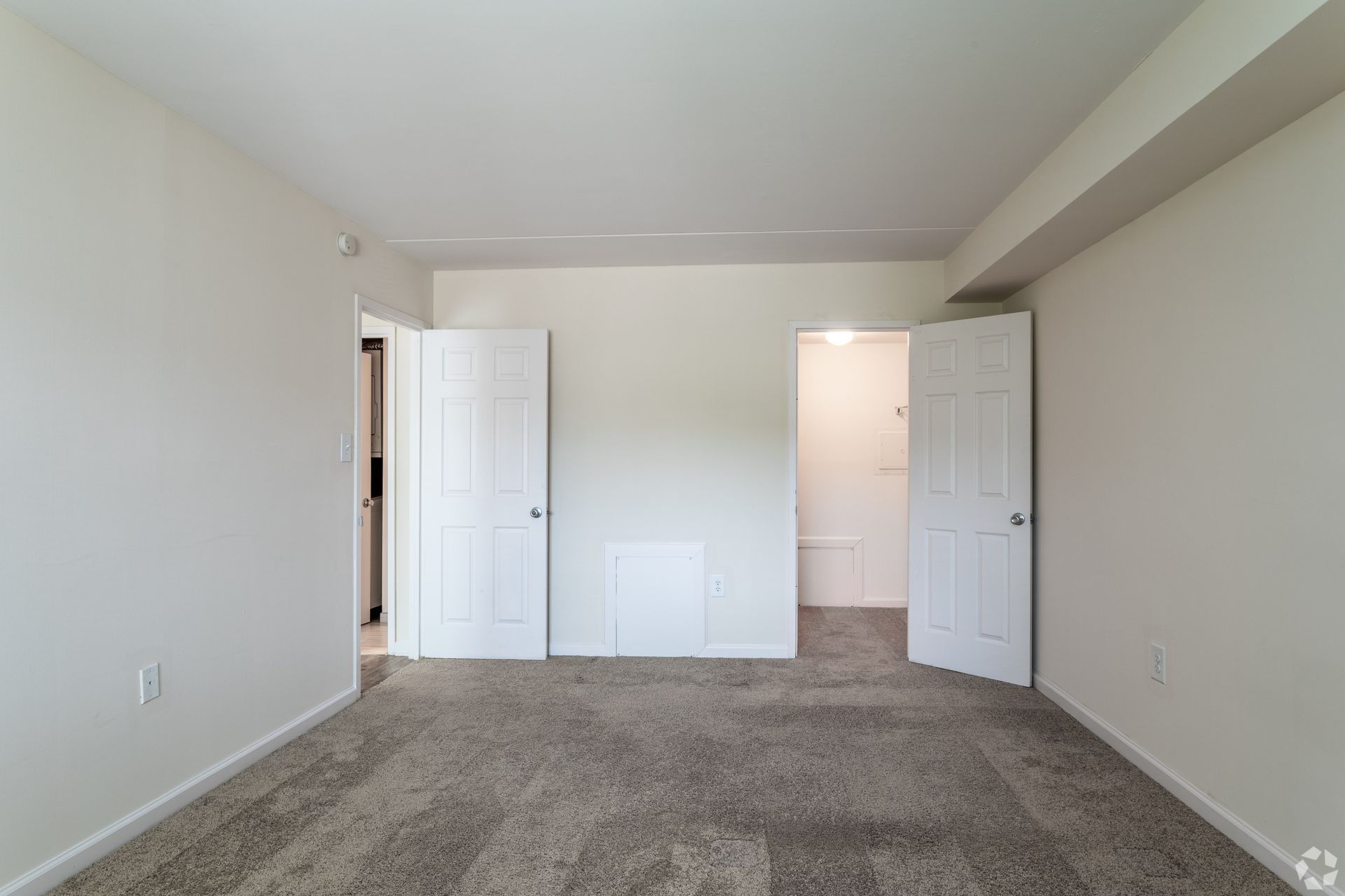 Empty bedroom with carpet, two white doors, and a bathroom doorway.