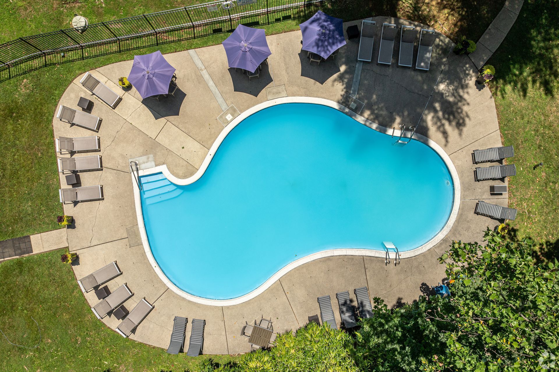 Aerial view of a swimming pool with lounge chairs and blue umbrellas on a sunny day.
