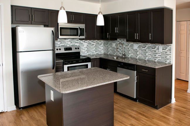 Modern kitchen with dark brown cabinets, stainless steel appliances, and a granite island.