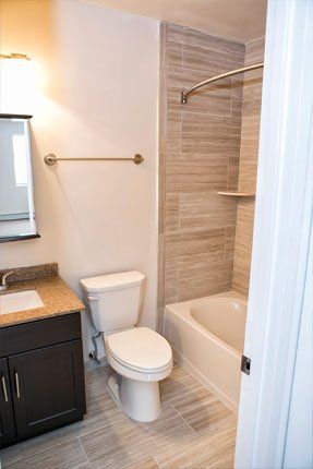Bathroom with toilet, vanity, and bathtub. Beige tile on the floor and wall. White door is on the right side.