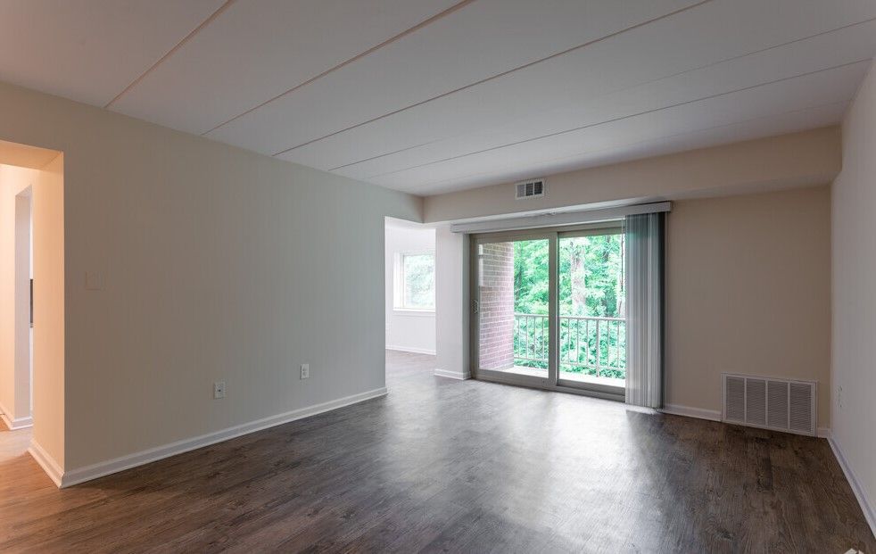 Empty living room with wood-look flooring, balcony door, and an entryway.