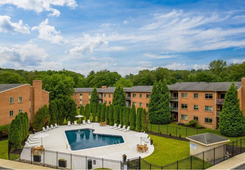 Apartment complex with a pool, trees, and blue sky.