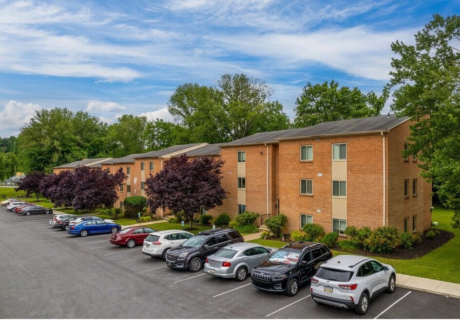 Apartment building with cars parked in front under a partly cloudy sky.