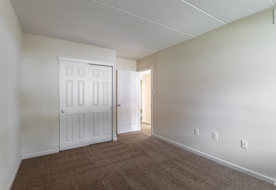 Empty bedroom with tan carpet, white walls, closet doors, and doorway.
