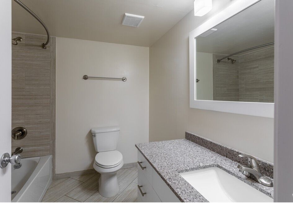 Bathroom with a white vanity, toilet, and bathtub with a tiled shower. Light-colored walls and floor.