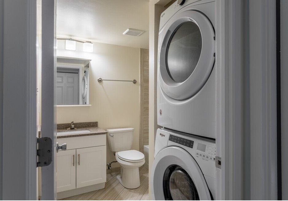Bathroom with stacked washer/dryer, toilet, sink, mirror, and towel rack.