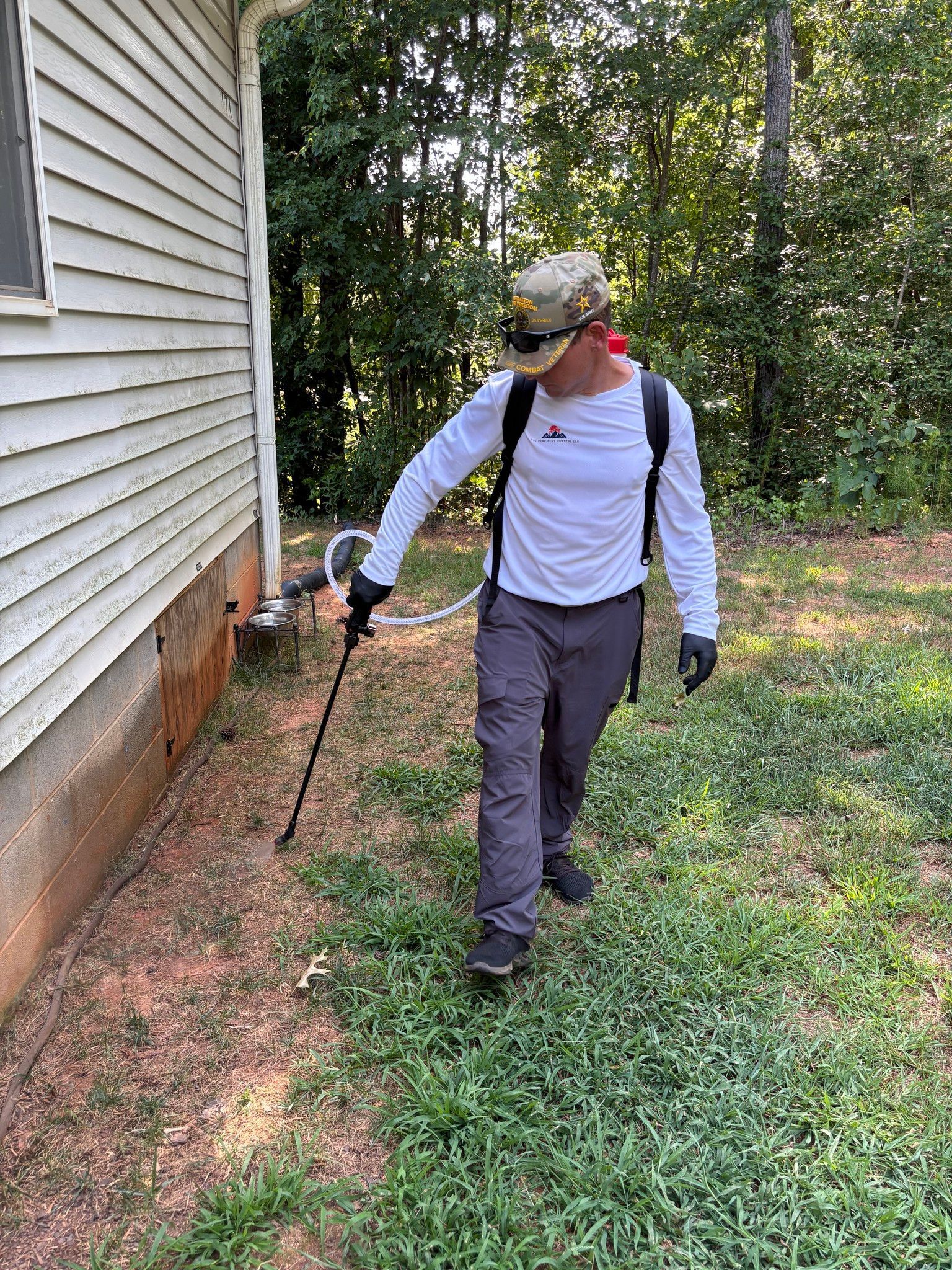 Person spraying insecticide along the foundation of a house.