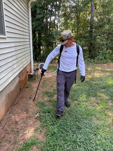 Person spraying insecticide along the foundation of a house.