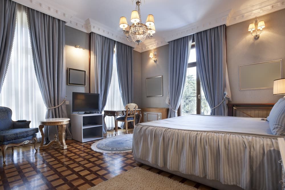 Elegant Bedroom with Blue Curtains, a Chandelier and A Small Table and Chair Are Visible — U Curtains in Acacia Ridge, QLD