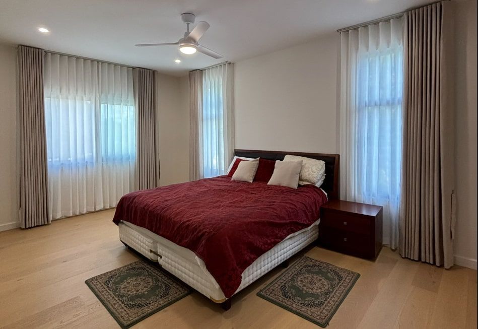 A Bedroom with A Bed Covered in A Red Comforter and Framed by Windows — U Curtains in Acacia Ridge, QLD