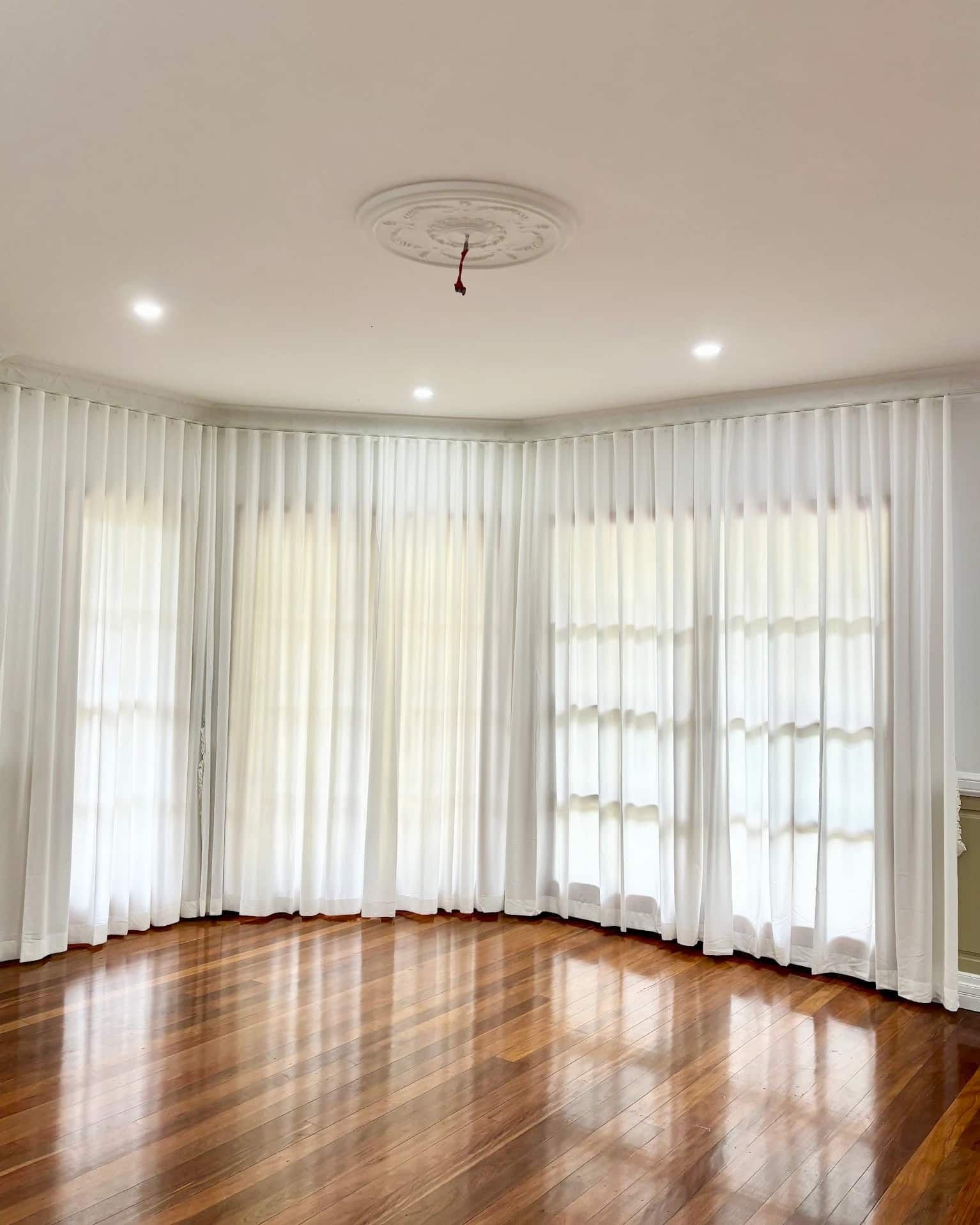 A Bright Empty Room with Curved Windows Draped in White Curtains Over a Polished Wooden Floor — U Curtains in Acacia Ridge, QLD