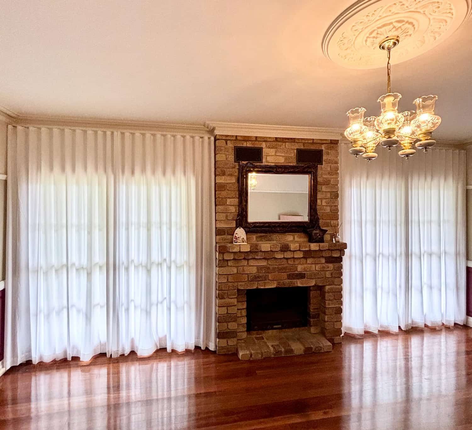 Living Room with A Brick Fireplace, Hardwood Floors and White Curtains Framing Large Windows — U Curtains in Acacia Ridge, QLD