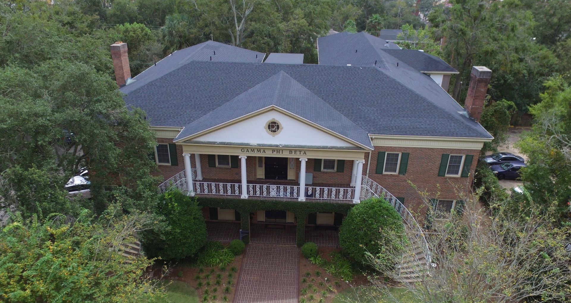 An aerial view of a large brick house with a black roof