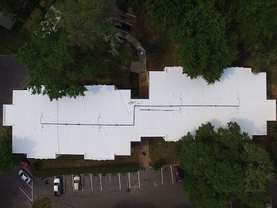 An aerial view of a building with a white roof surrounded by trees.