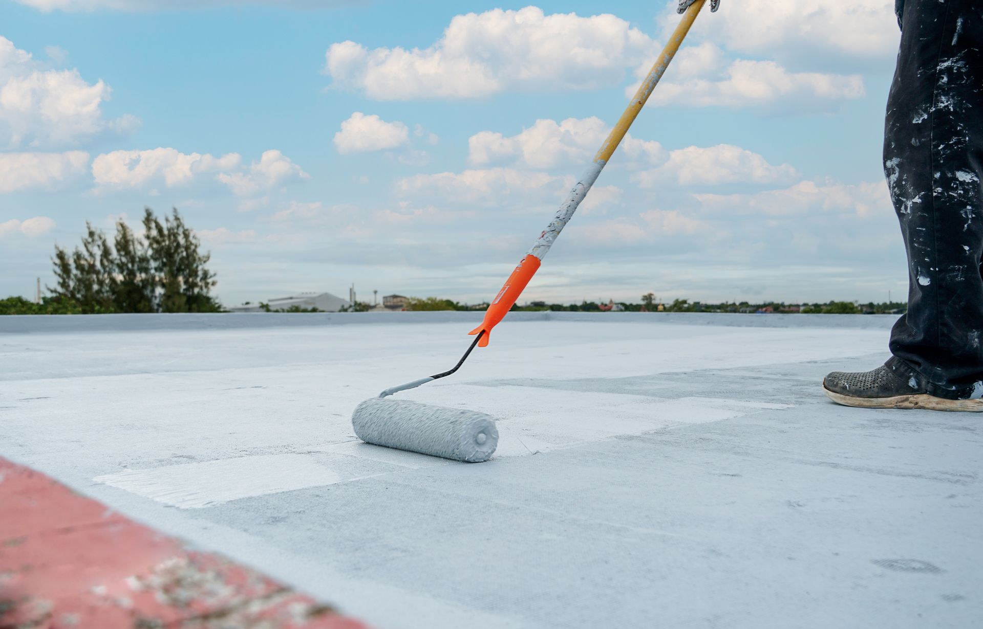A person is painting a roof with a roller.