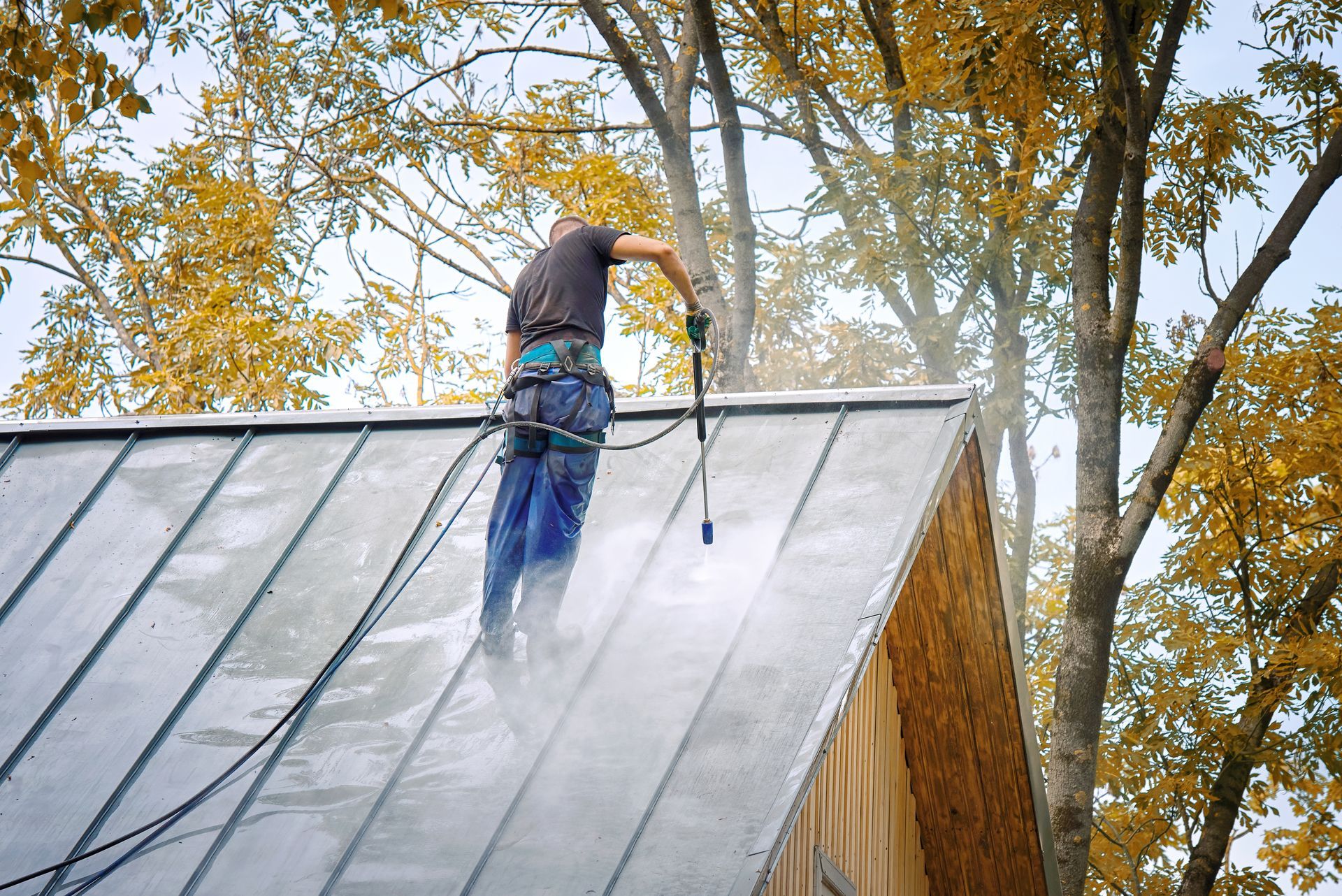 A man is cleaning the roof of a house with a high pressure washer.