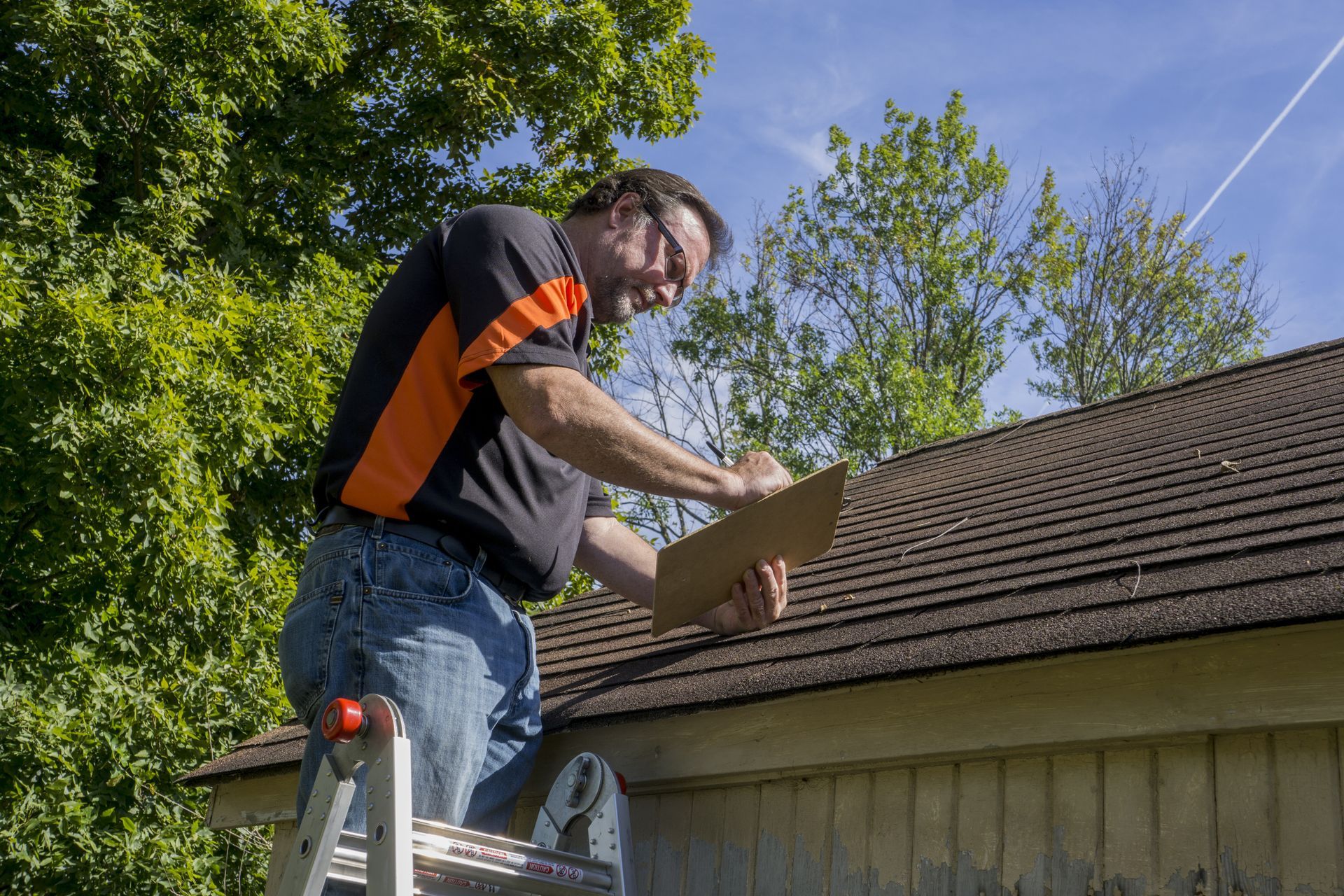 A man is sitting on a ladder looking at a clipboard.