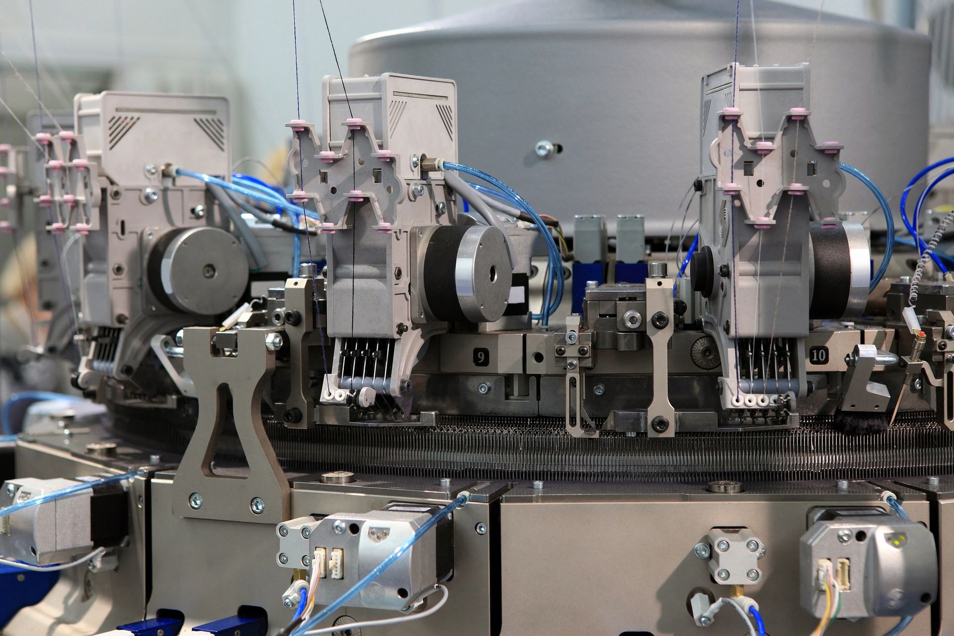 Primer plano de una máquina de tejer compleja con múltiples brazos mecánicos y partes móviles, probablemente para producción textil.