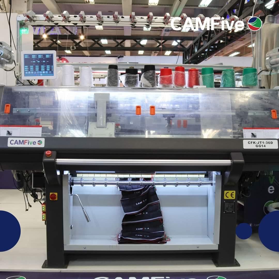 Una máquina de tejer computarizada CAMFive en una feria comercial, con una pieza textil terminada en primer plano.