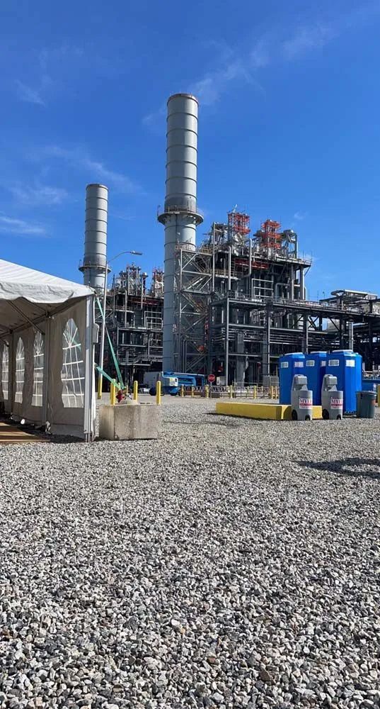 There is a tent in the middle of a gravel field in front of a large factory