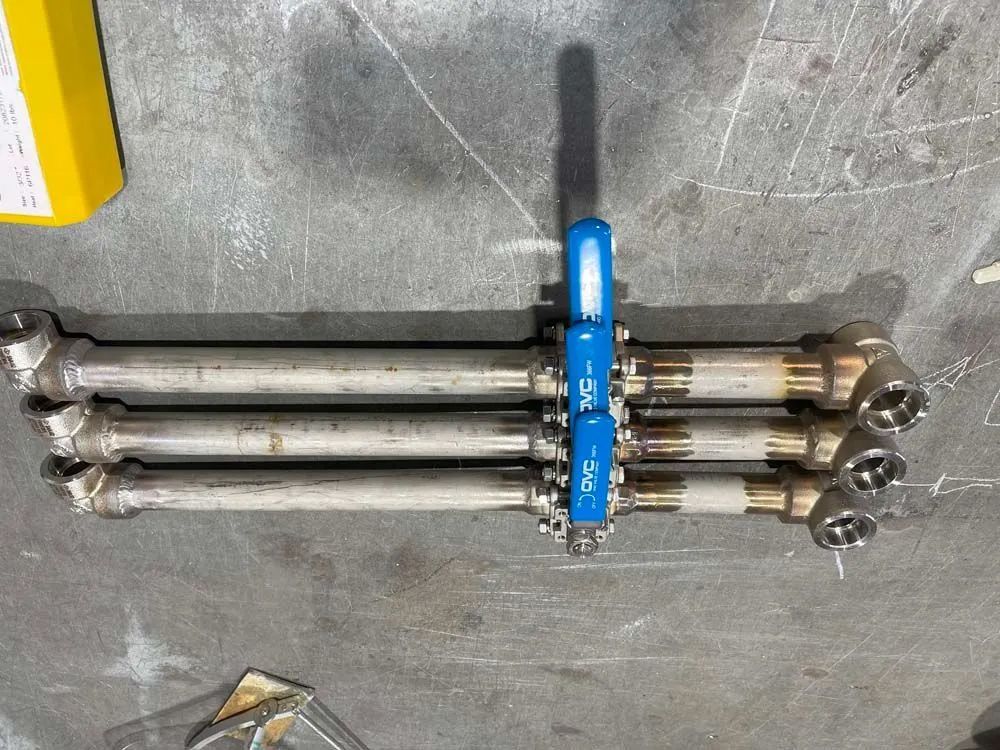 A stainless steel valve with a blue handle is sitting on a concrete surface