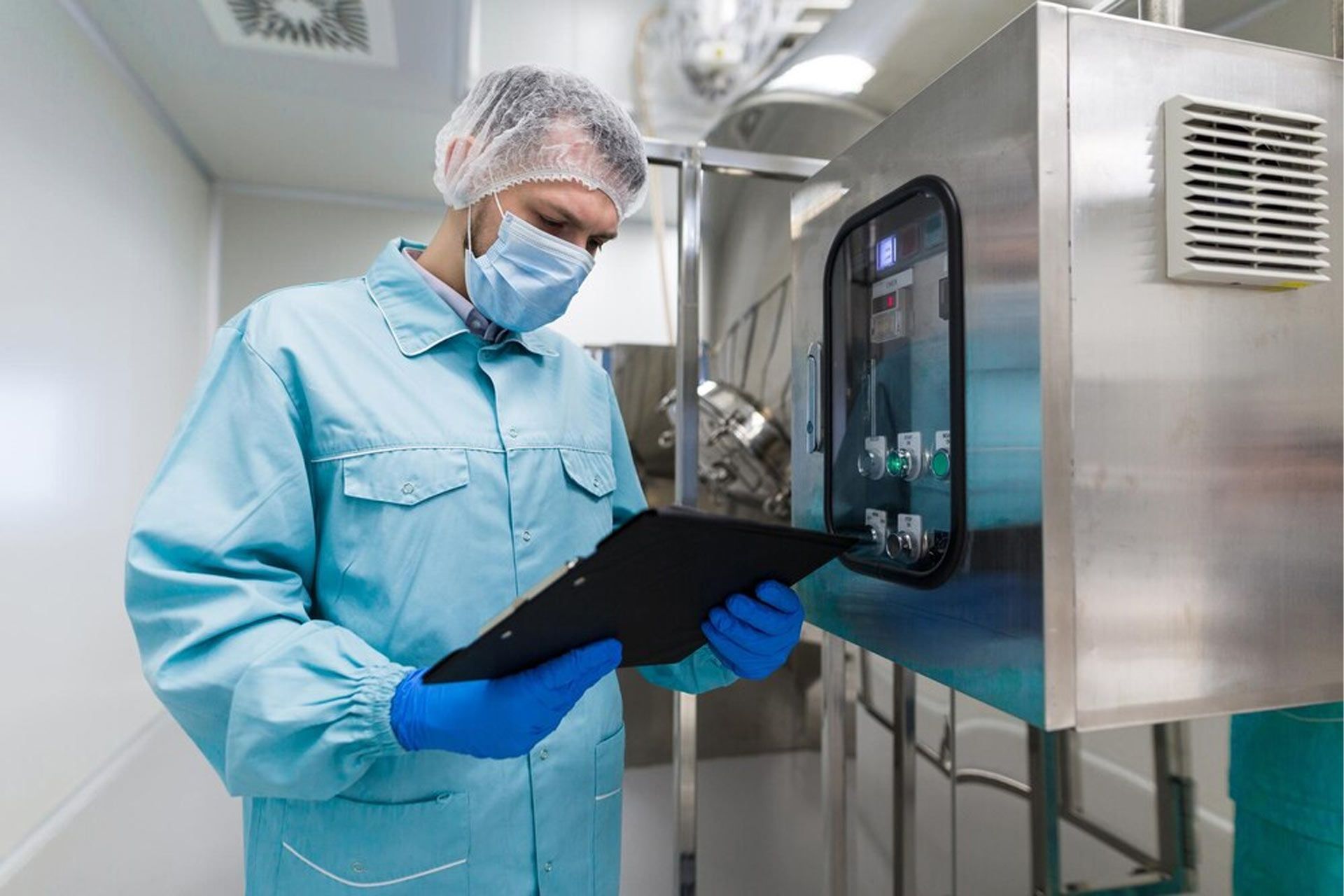 A scientist in a clean room is looking at a clipboard.