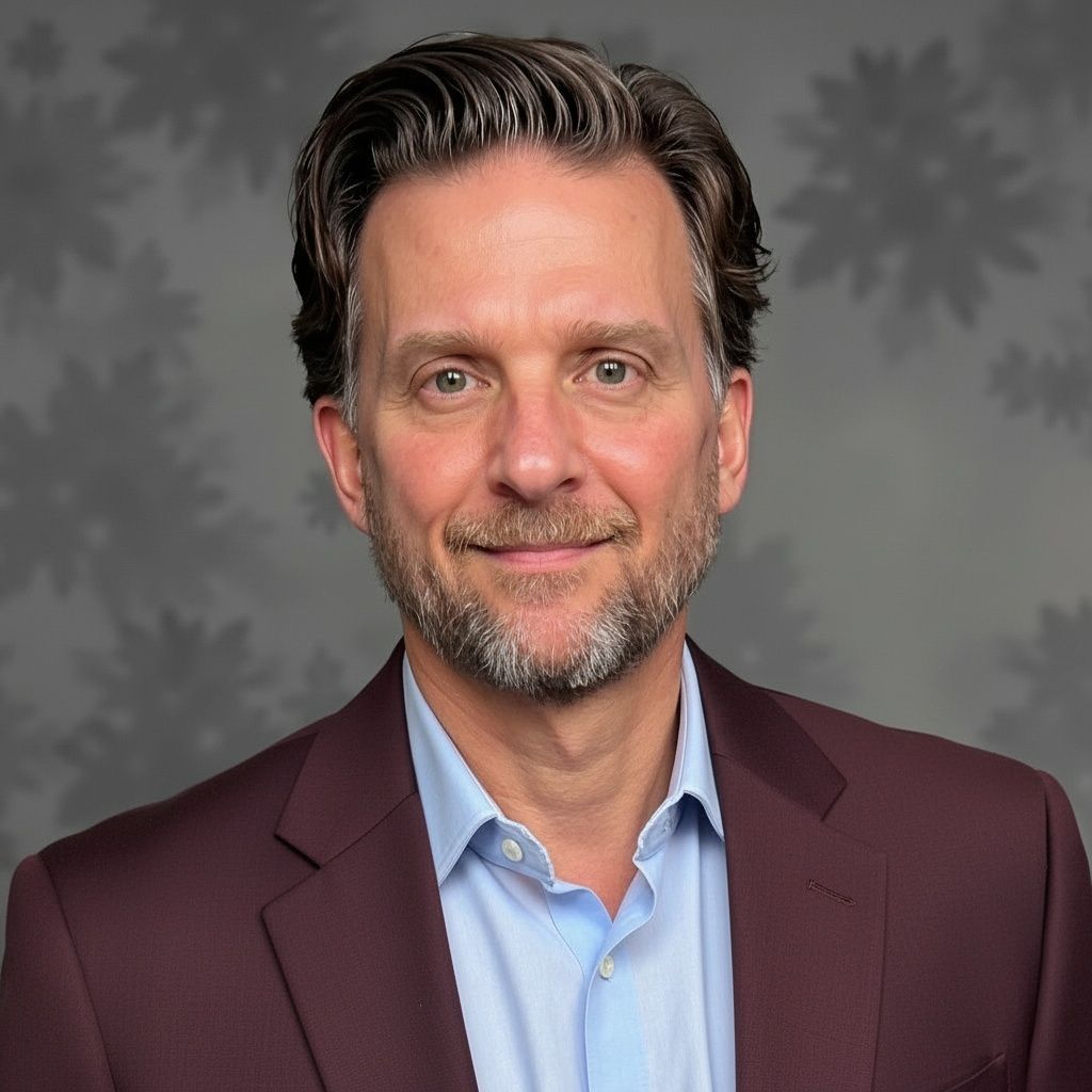 Man in a burgundy suit jacket and blue shirt, smiling at the camera against a patterned gray background.