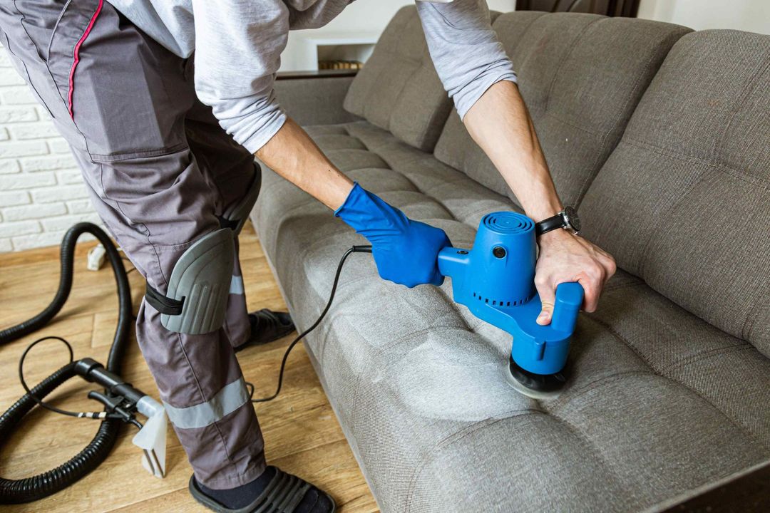 A man is cleaning a couch with a vacuum cleaner