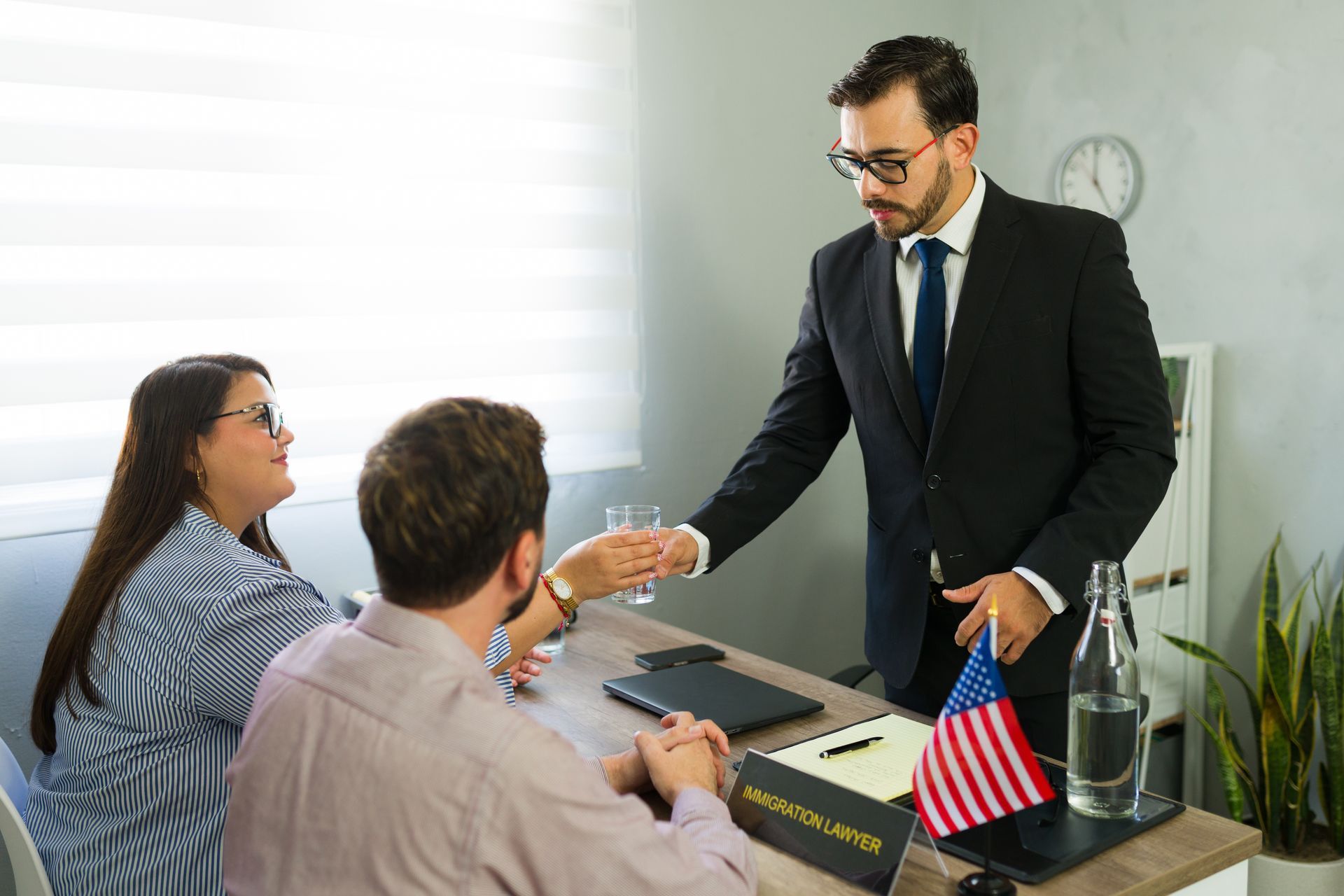 An immigration lawyer meets clients in an office with a flag and clock visible.