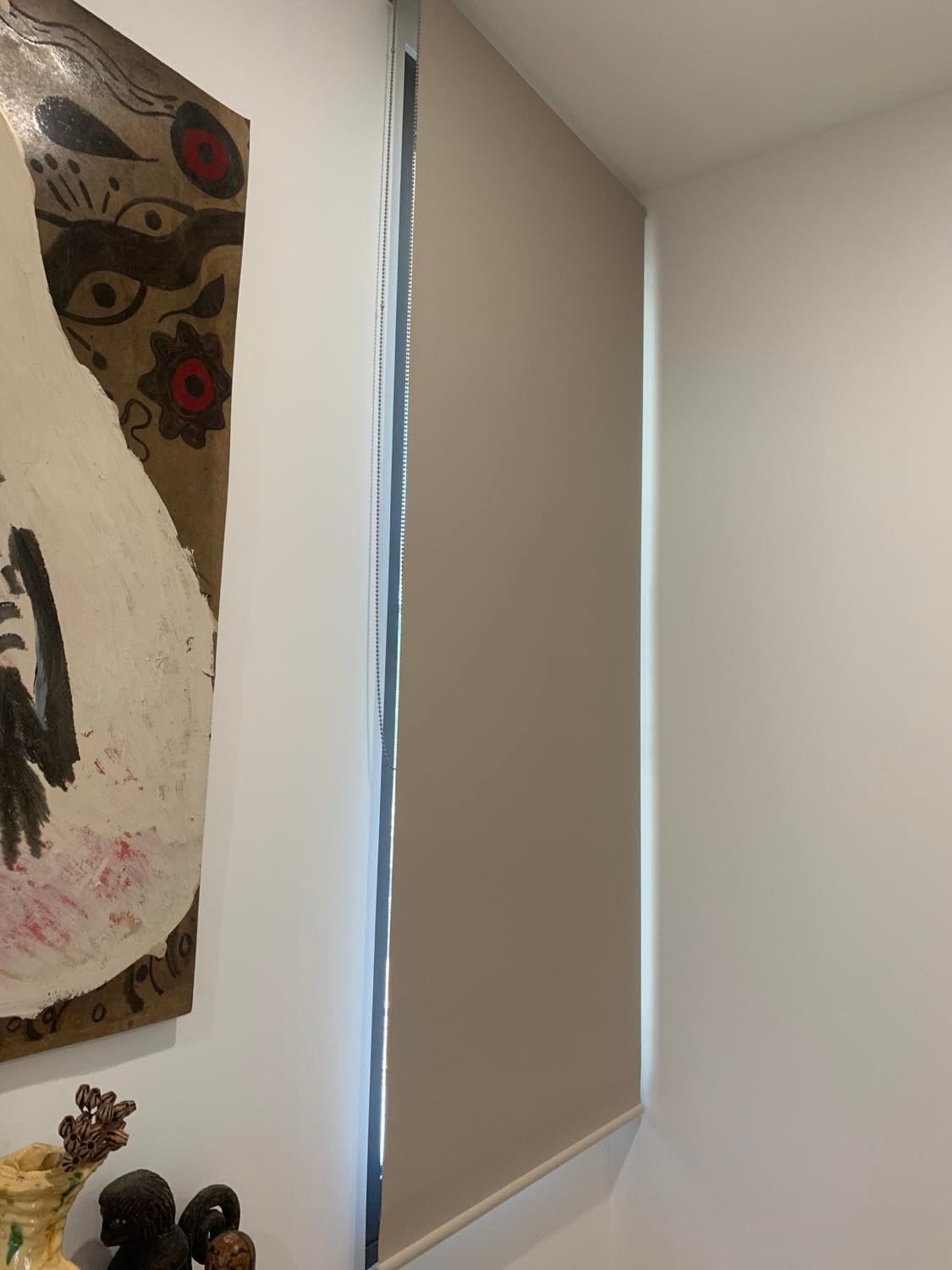 Beige Roller Blind Next to A White Wall with Artwork and A Small Cabinet — Alice Mobile Blinds in Ciccone, NT