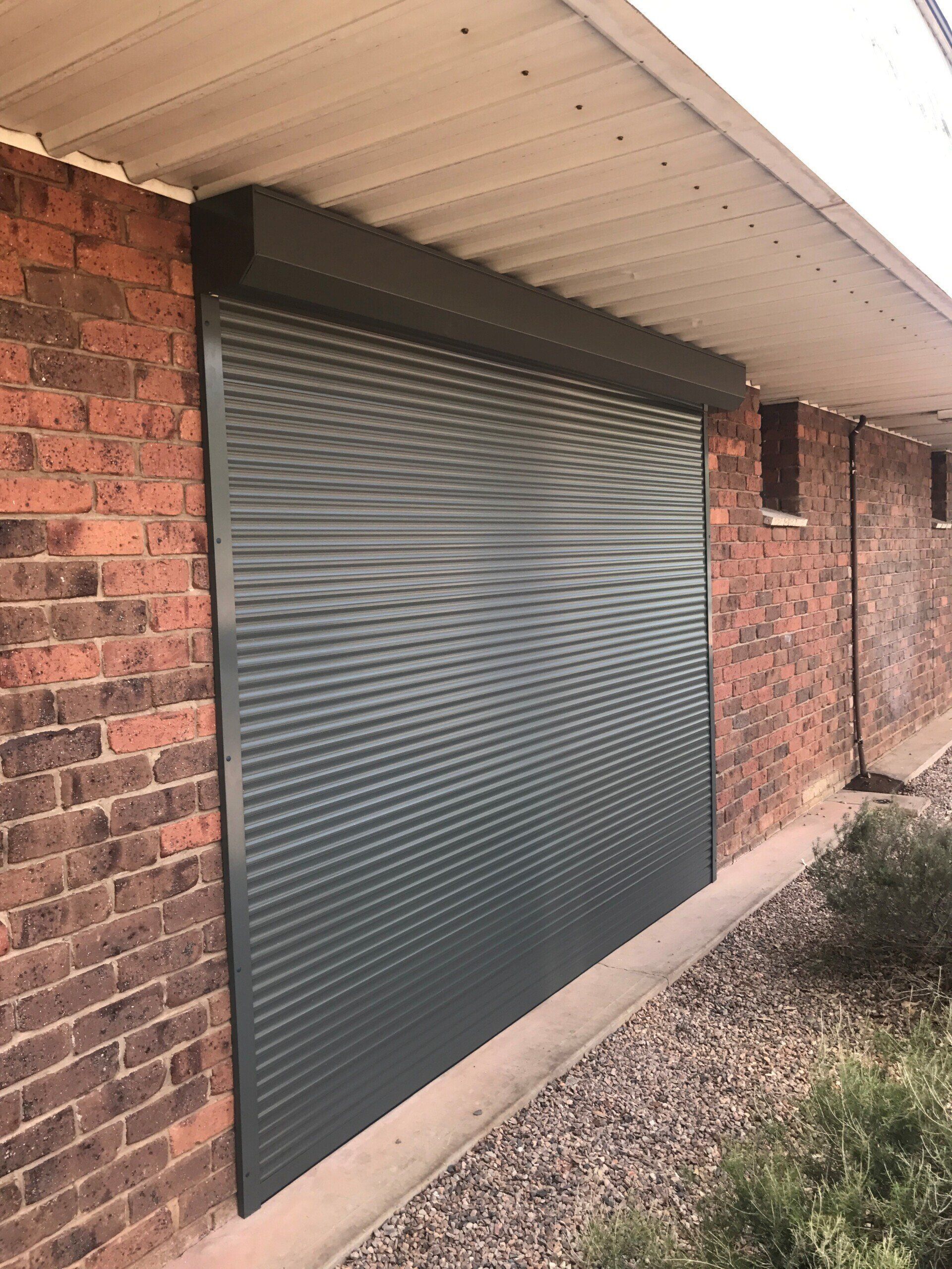 Dark Grey Roller Shutter Installed on A Red Brick Building — Alice Mobile Blinds in Ciccone, NT