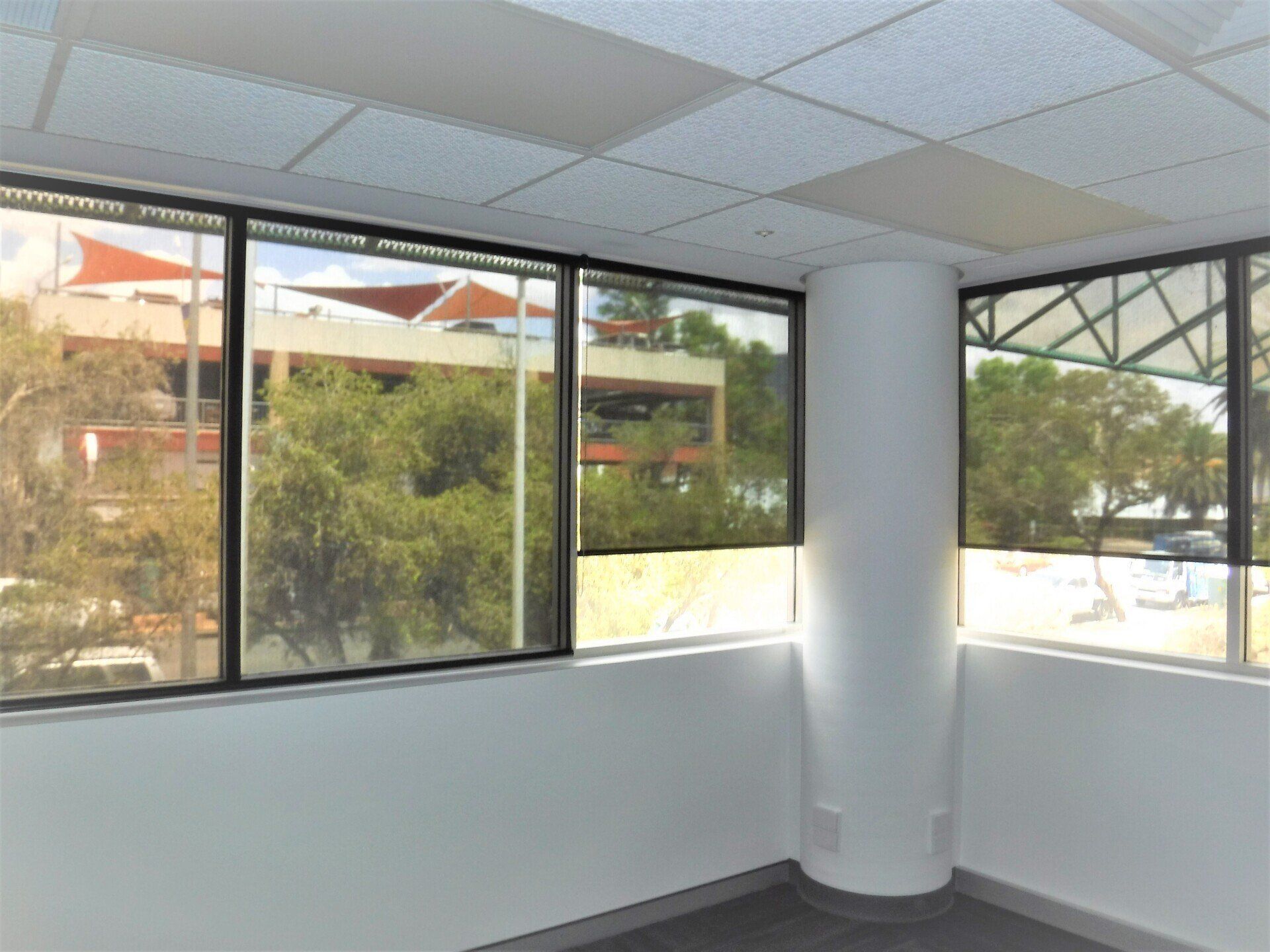 Empty Office Corner with Windows Overlooking Greenery and Buildings — Alice Mobile Blinds in Ciccone, NT