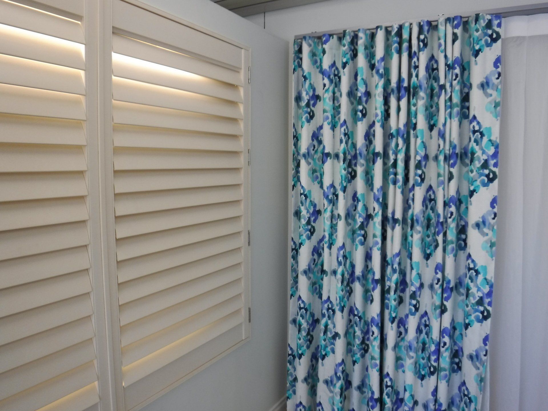 Cream-Coloured Shutters Next to Blue and White Patterned Curtains — Alice Mobile Blinds in Ciccone, NT