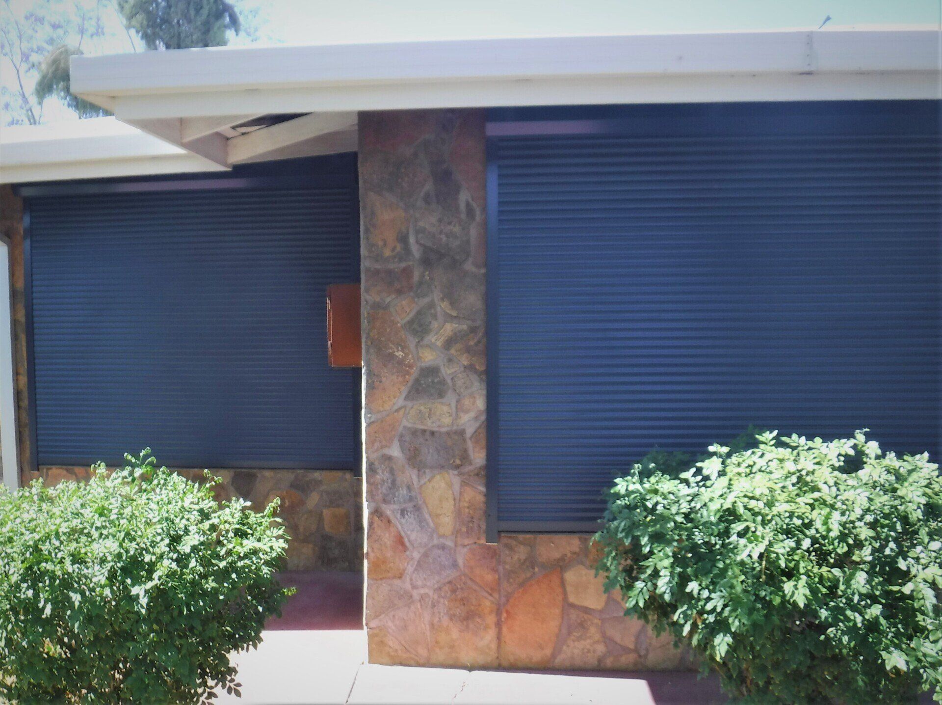 Exterior View of A House with Two Windows Covered by Blue Rolling Shutters — Alice Mobile Blinds in Ciccone, NT