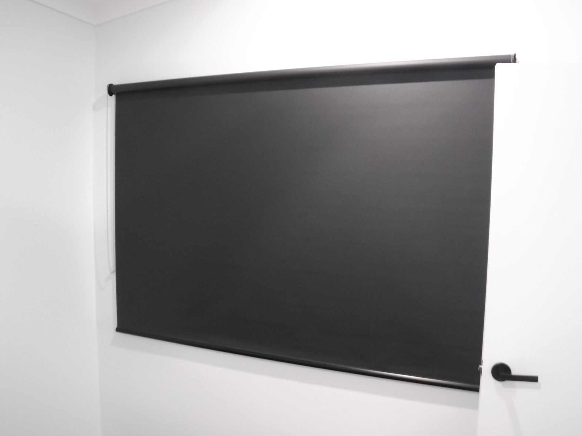 Black Roller Blind Covering a Window in A White-Walled Room — Alice Mobile Blinds in Ciccone, NT