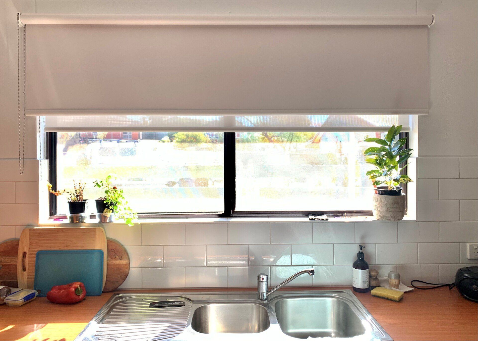 Kitchen Window with White Blinds Above a Stainless Steel Sink and Countertop — Alice Mobile Blinds in Ciccone, NT