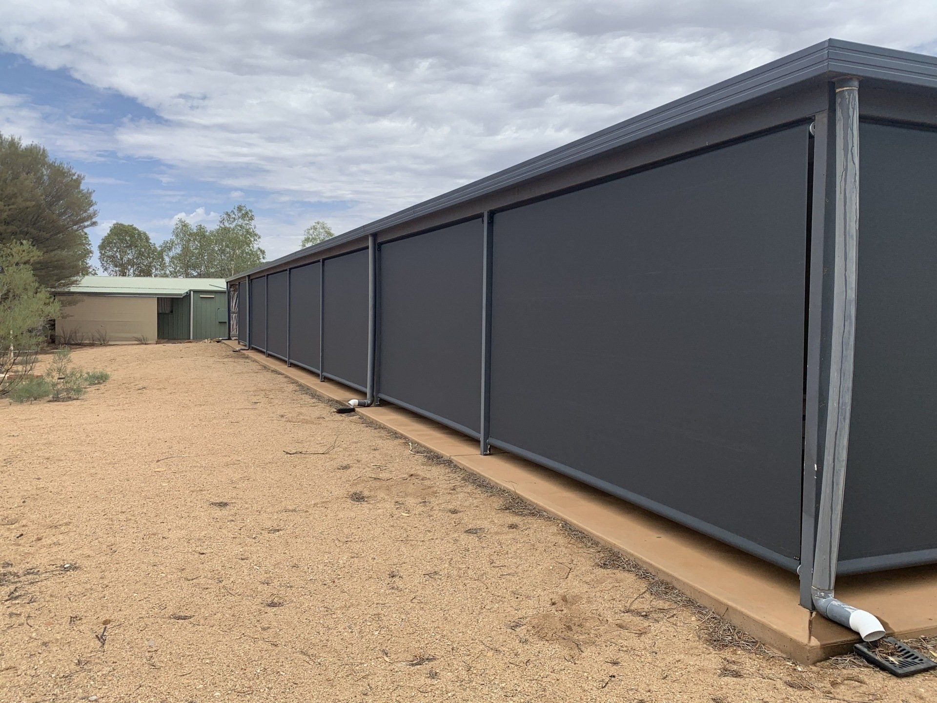 Dark Grey Outdoor Blinds Attached to A Long Low Structure — Alice Mobile Blinds in Ciccone, NT