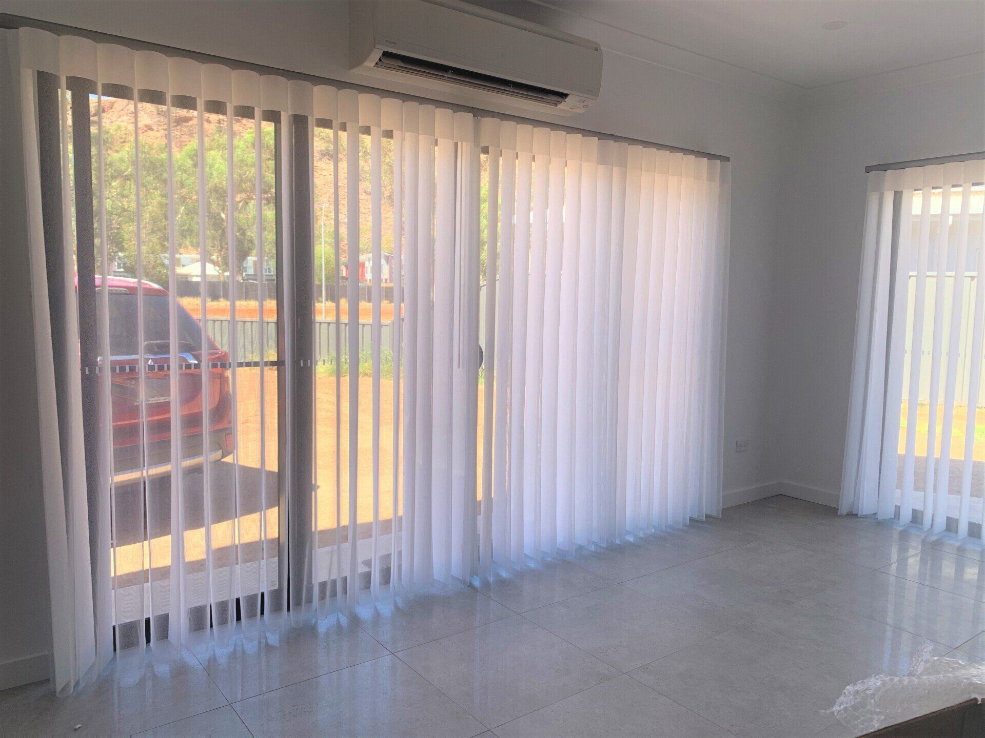 Room with White Vertical Blinds, Sliding Glass Door and An Air Conditioner — Alice Mobile Blinds in Ciccone, NT