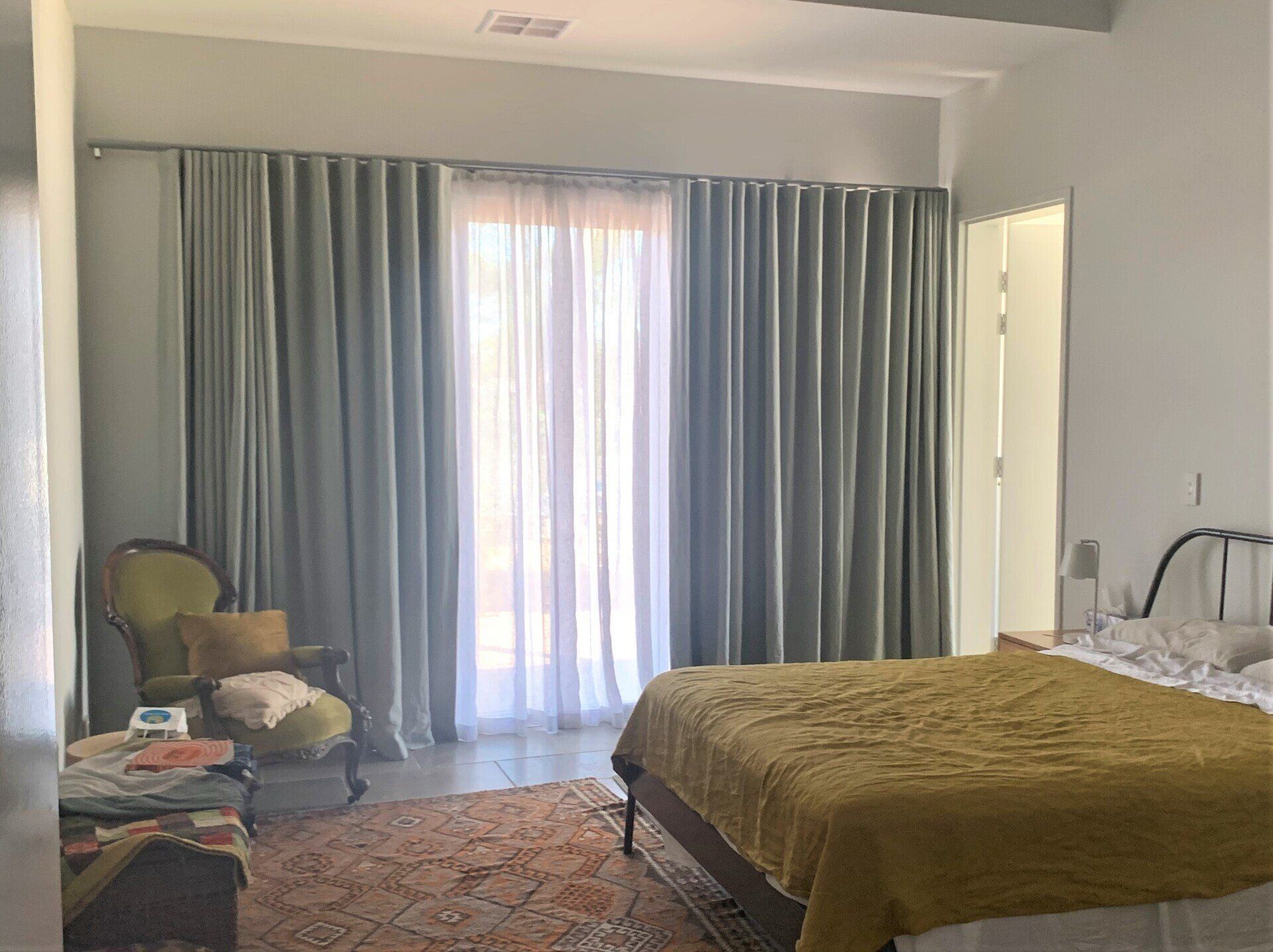 Bedroom with Grey Curtains, Bed, Chair and Rug — Alice Mobile Blinds in Ciccone, NT