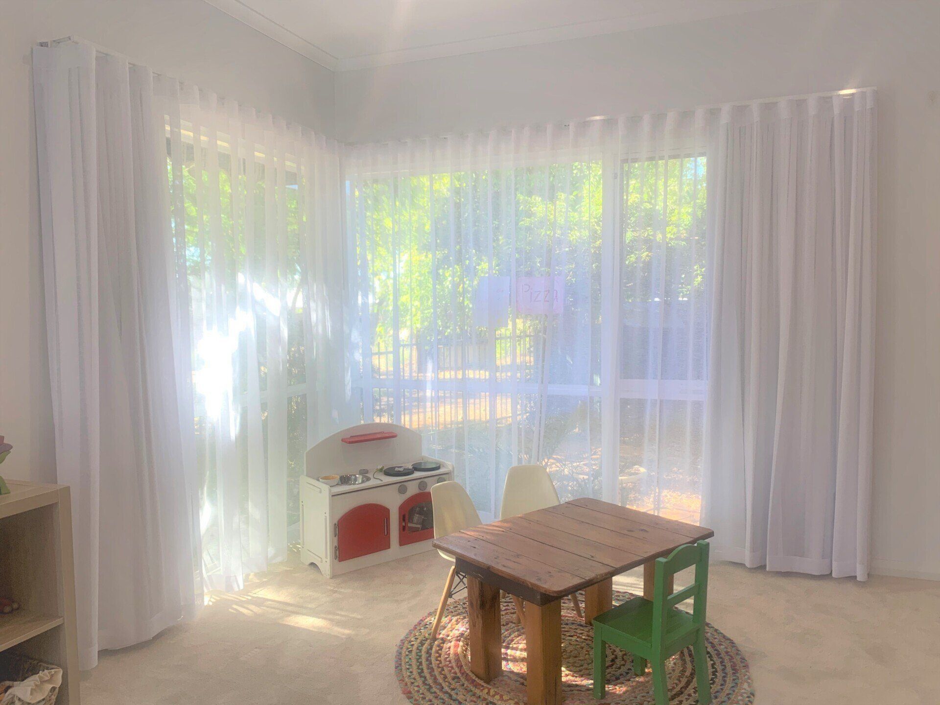 White-Curtained Playroom Corner with A Small Wooden Table — Alice Mobile Blinds in Ciccone, NT