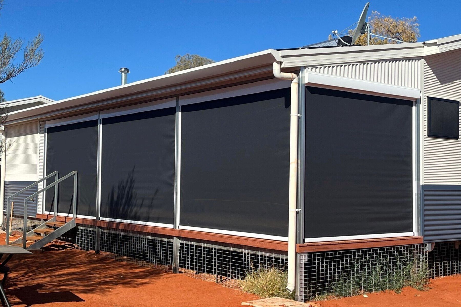 Black Outdoor Roller Blinds Installed on A Light-Coloured Building with A Porch — Alice Mobile Blinds in Ciccone, NT