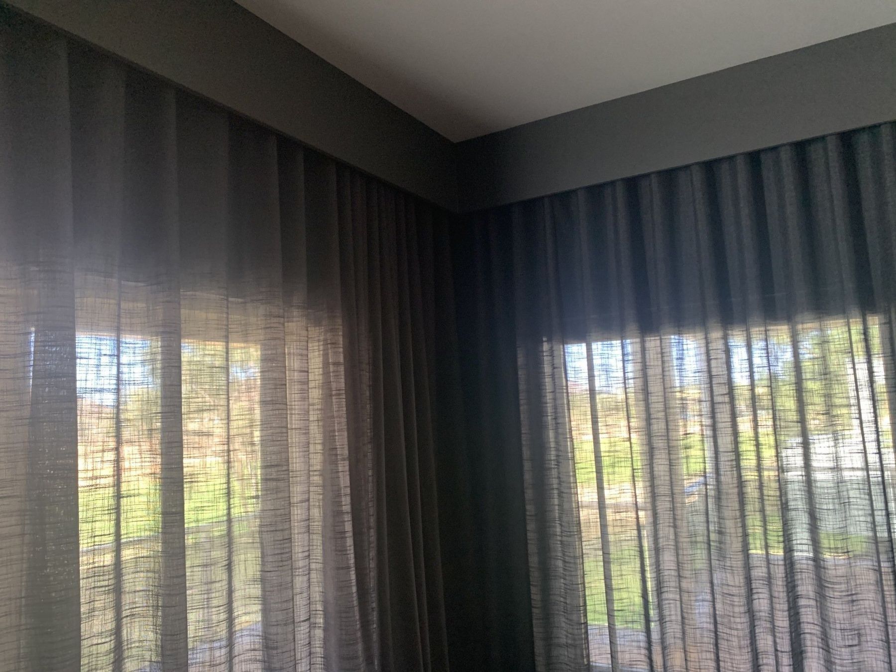 Dark Grey Sheer Curtains Frame a Corner Window — Alice Mobile Blinds in Ciccone, NT