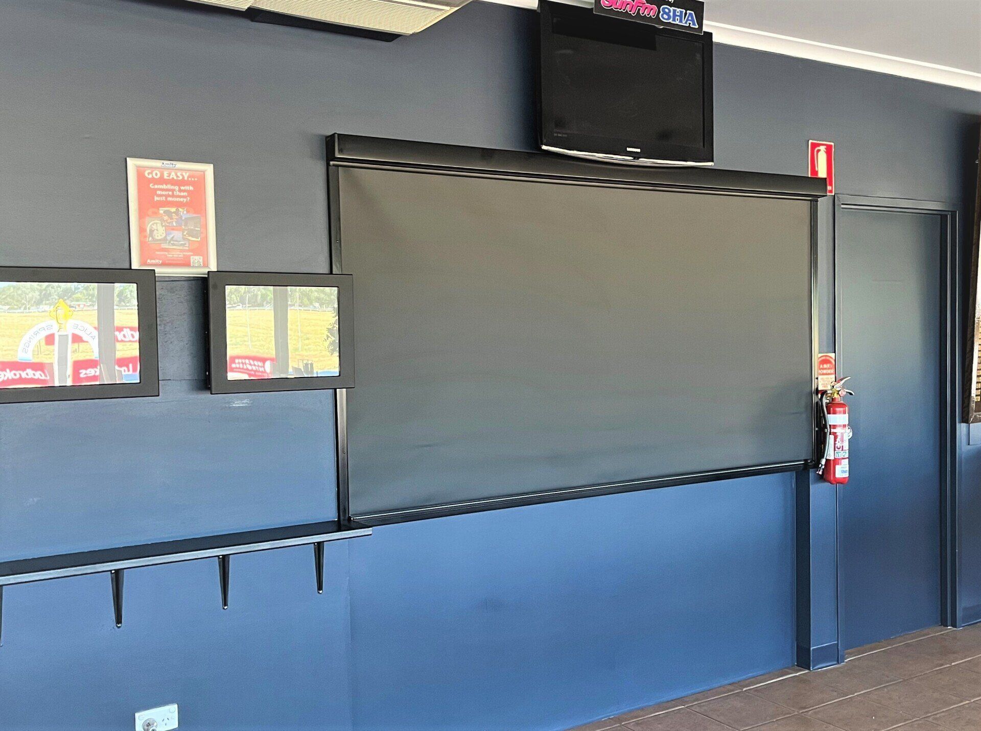 Blue Wall with Two Framed Posters, a Large Screen and Fire Extinguisher — Alice Mobile Blinds in Ciccone, NT
