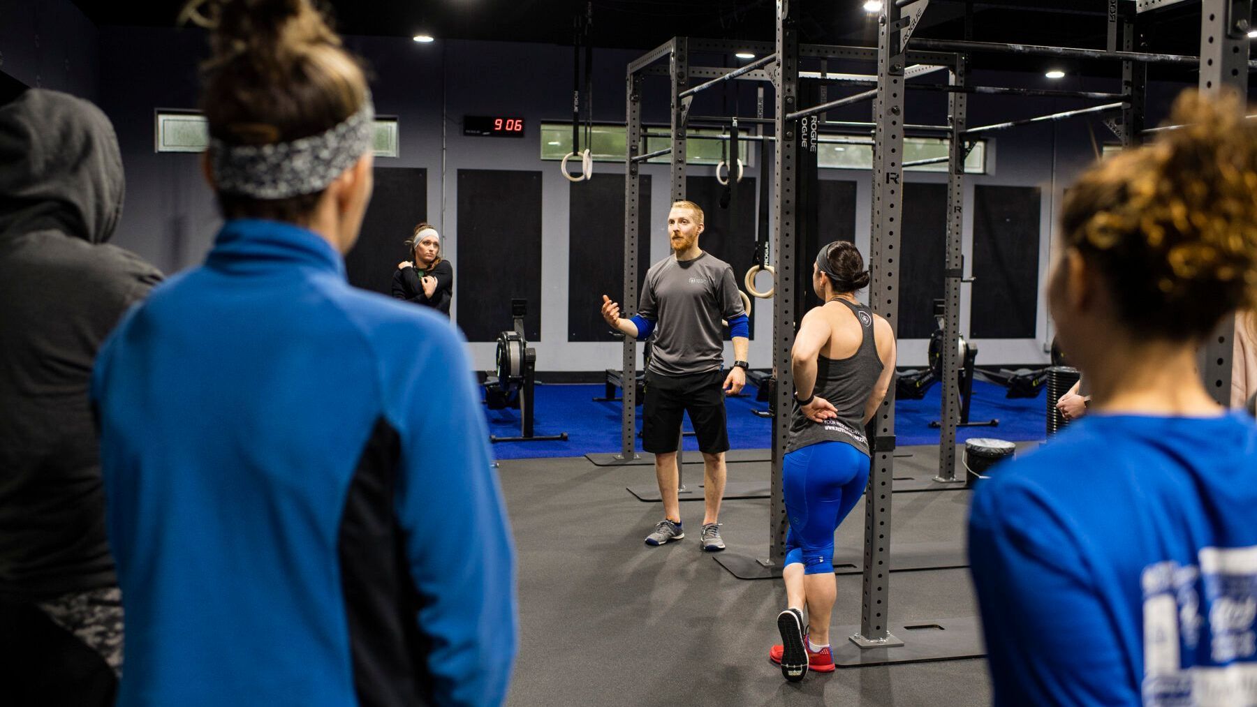 A group of people are standing in a gym listening to a man talking.