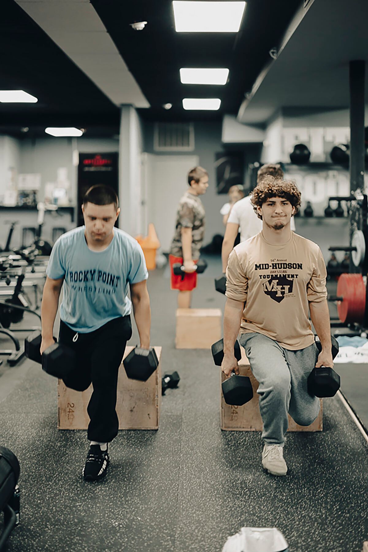 Two men are doing lunges with dumbbells in a gym.