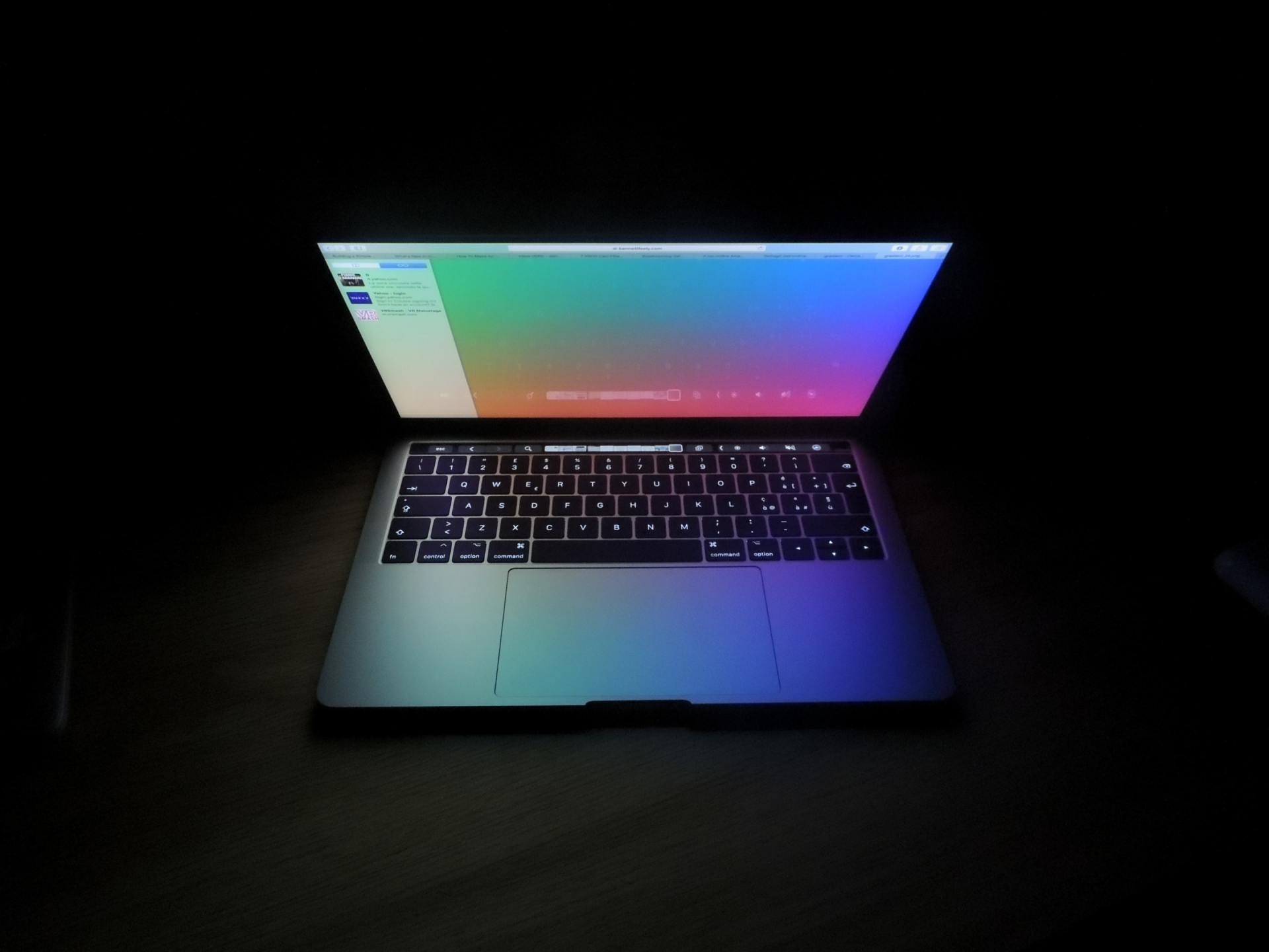 Ein Laptop mit einem regenbogenfarbenen Bildschirm ist im Dunkeln geöffnet