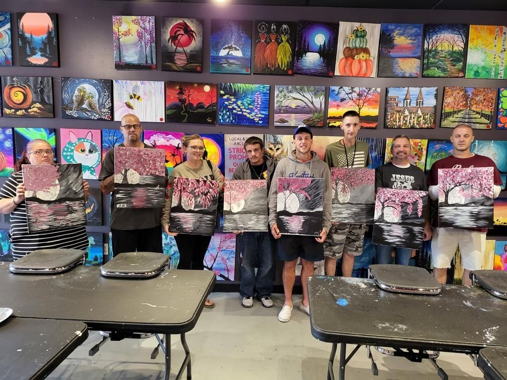 A group of people are standing in front of a wall holding paintings.