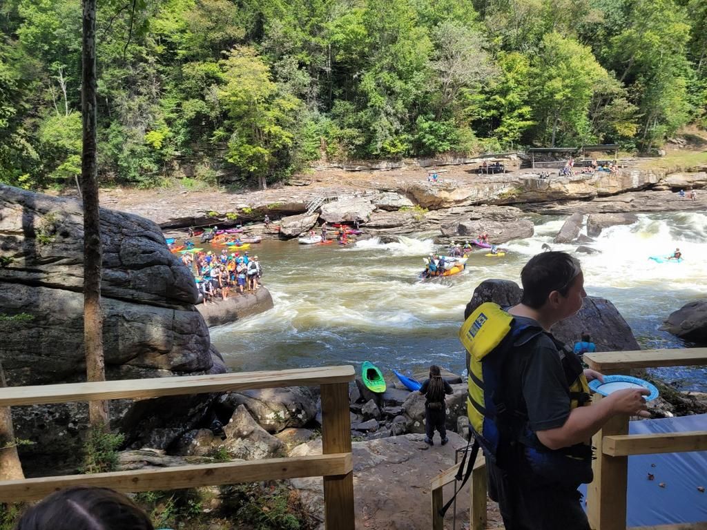 A man in a life jacket is standing on a bridge overlooking a river.
