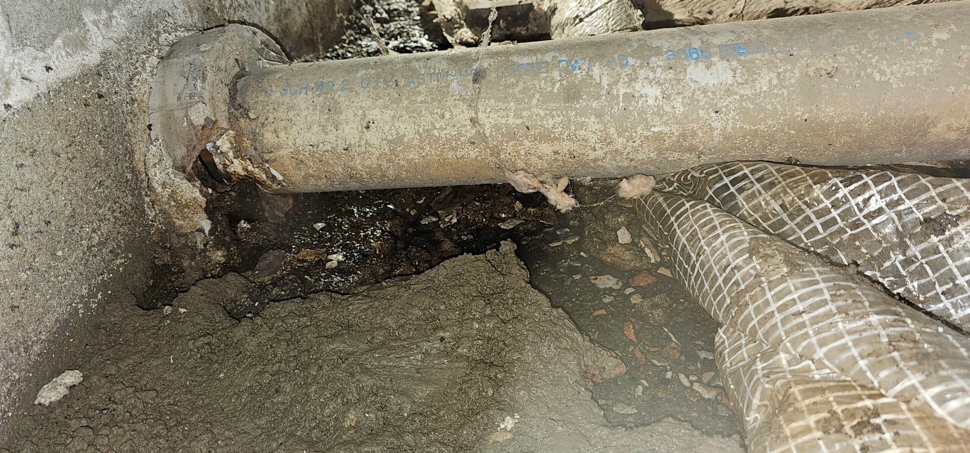 Corroded pipes in a damp, gritty environment with exposed insulation.
