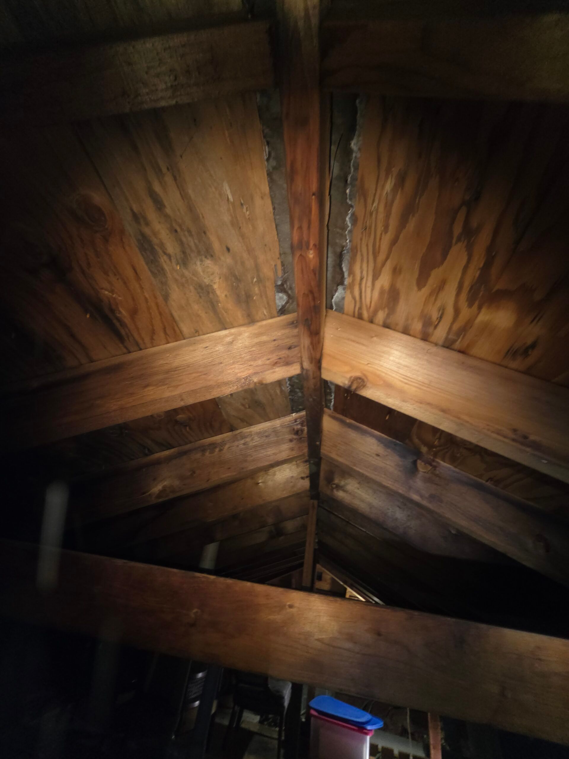 Wooden attic ceiling with beams meeting at a peak. Dark wood is visible, with light streaks.
